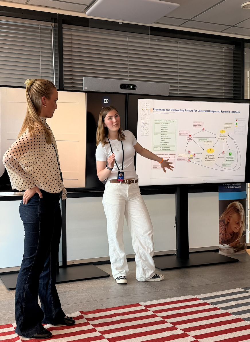 Two researchers presenting the relational GIGA-map on a large screen in a Telenor meeting room.