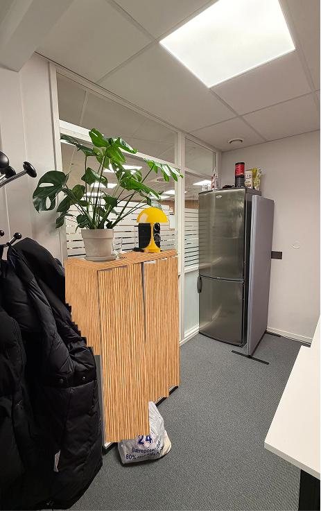 A Gr&uuml;ndergarasjen work room as proposed, with a plant on a cabinet, coats hanging by the door and a fridge.